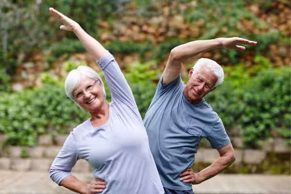 Two smiling older adults stretching outdoors as part of a regular exercise routine to support diabetes care.