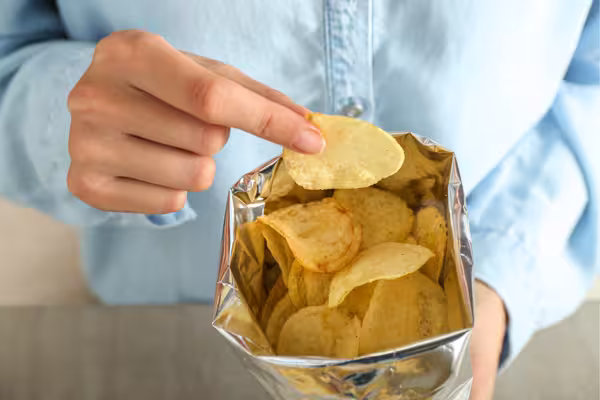 Hand reaching into a bag of potato chips, highlighting the lack of portion control risky for diabetes.